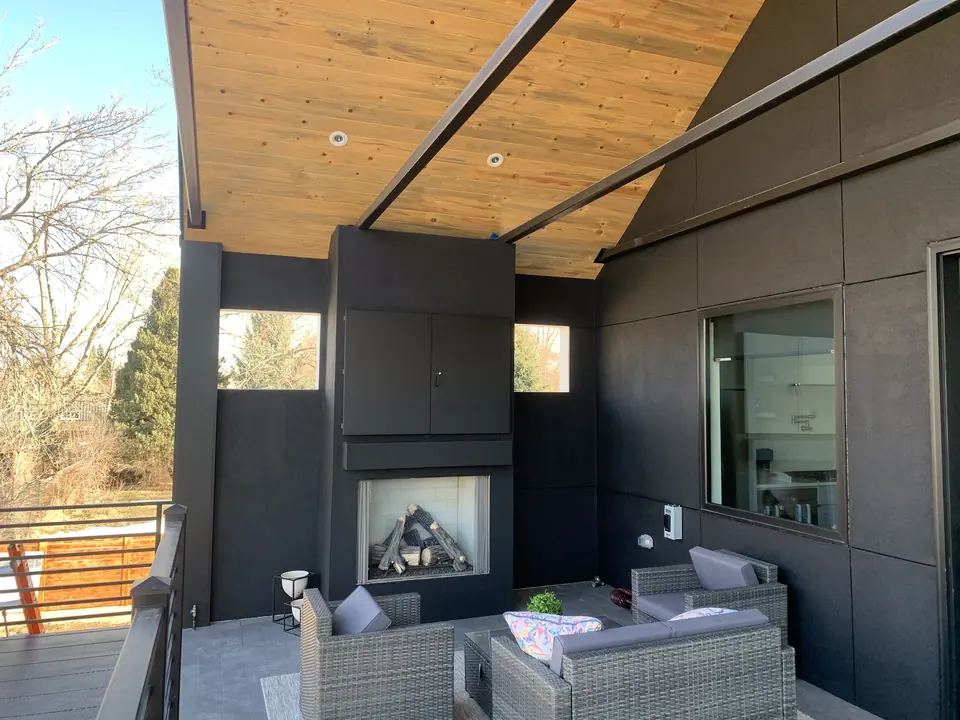 Covered outdoor patio with dark steel-clad walls, fireplace and lounge seating