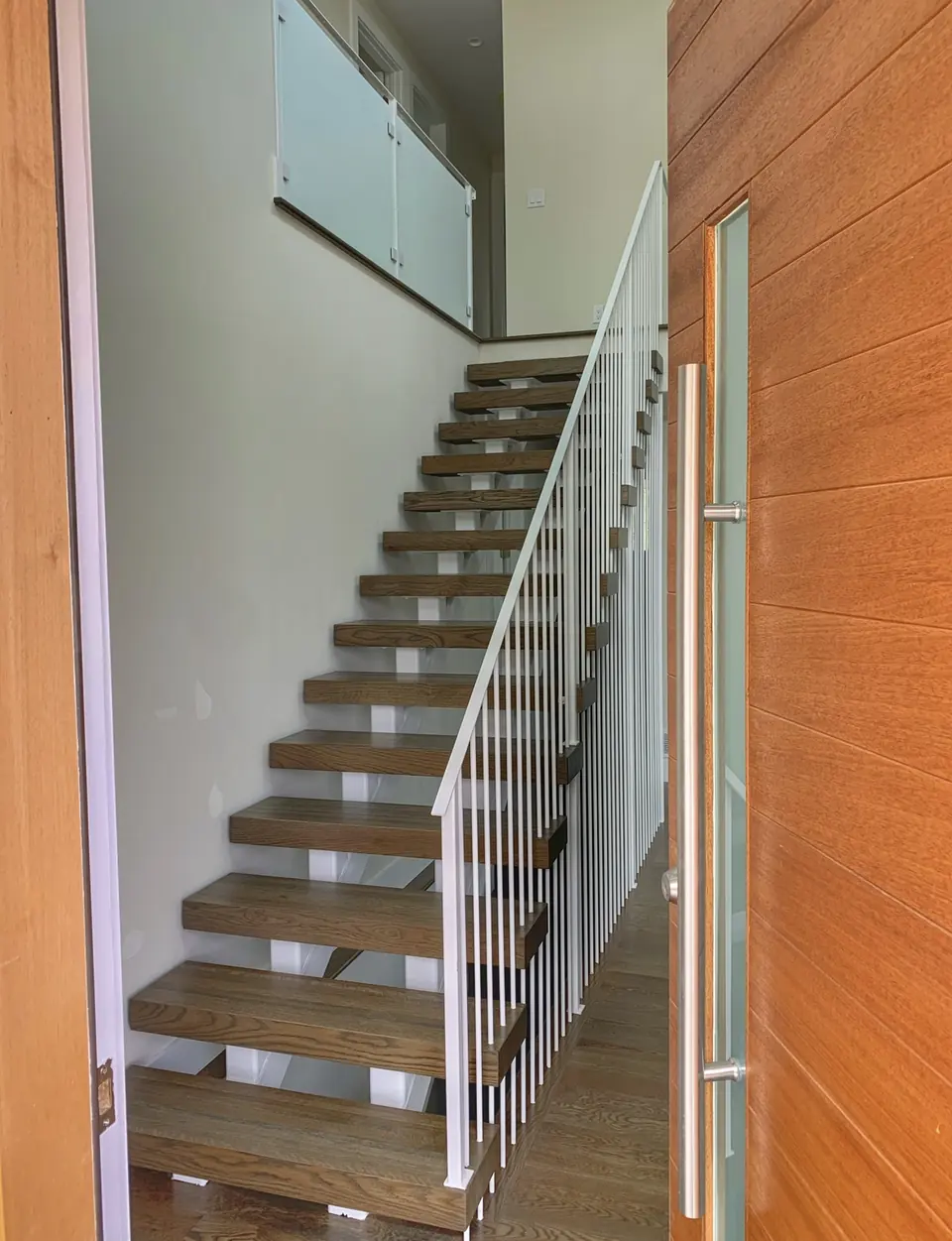 Interior wood stair with a white steel picket guardrail and wall-mounted handrail