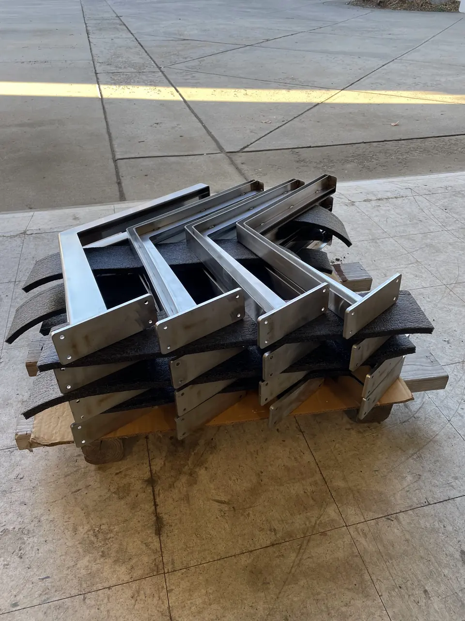 Stack of fabricated stainless steel brackets on a pallet in the shop