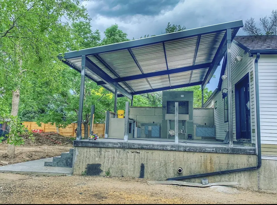 Steel-framed patio cover structure built over a raised concrete deck beside a house