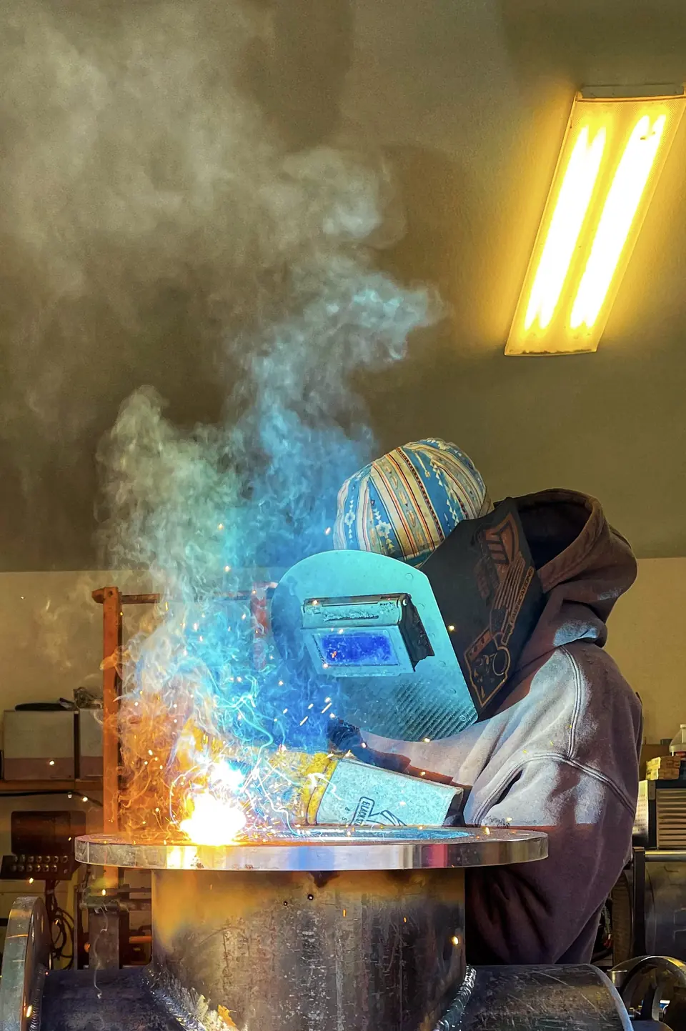 Welder fabricating a flanged steel assembly in the SteelCraft shop, sparks and smoke rising